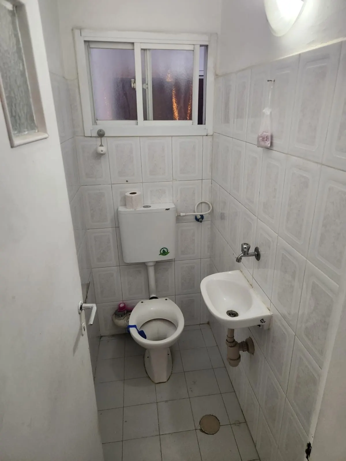 חדר שירותים ישן עם אסלה נמוכה ואריחים לבנים